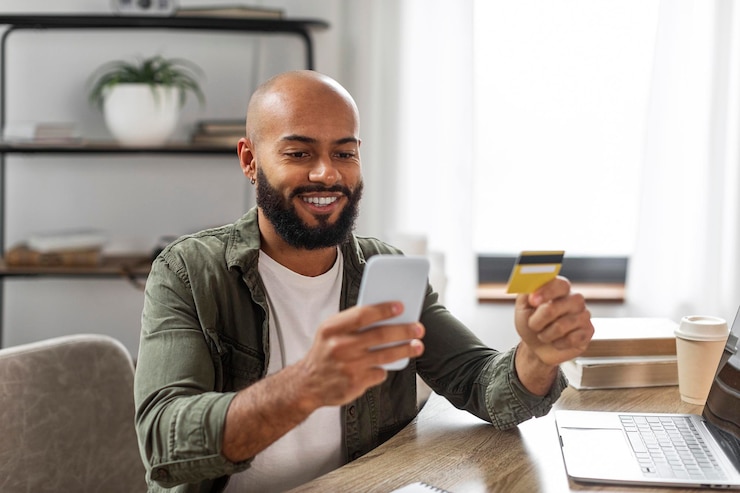 Photo buy and pay at home happy mature latin man using smartphone and credit card shopping online sitting at desk at home