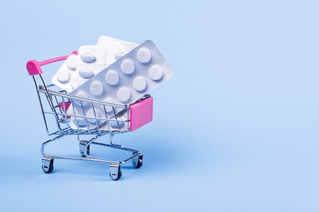 Buy and shopping medicine concept. Various capsules, tablets and medicine in shop trolley on a blue background. Creative idea for health care, health insurance and pharmaceutical company. Copy space.