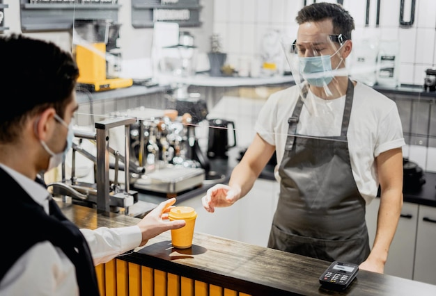 ウイルスに感染したマスク姿の若者とコーヒーを買う 街の小さな喫茶店