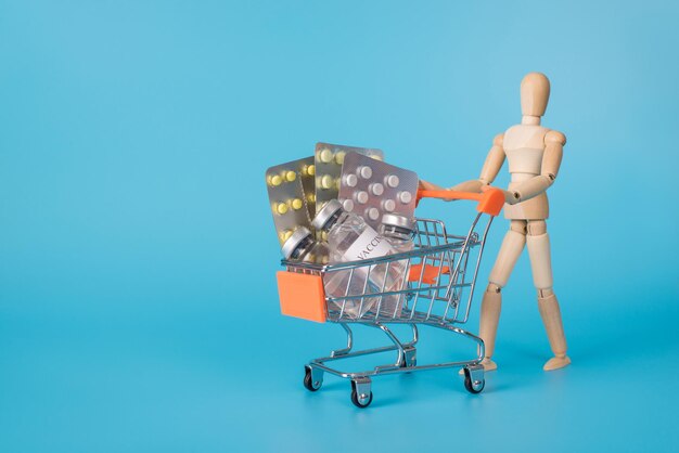 Buying drugs concept. Photo of wooden man carrying shopping cart full of different pharmaceutical pills isolated blue backdrop