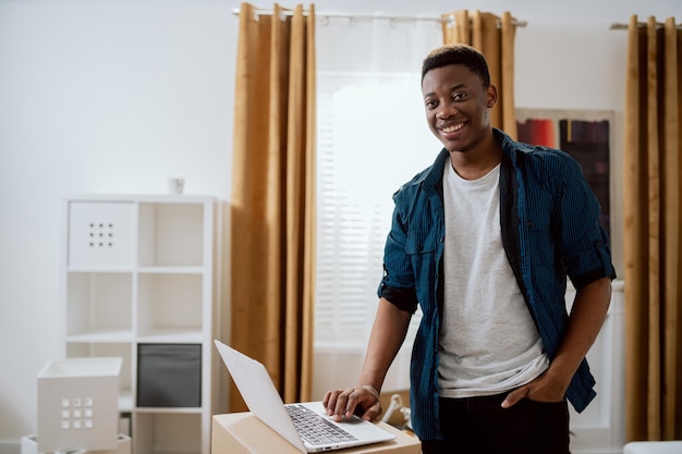 Buying furniture online a happy smiling man clicks on a laptop\
standing on cardboard boxes