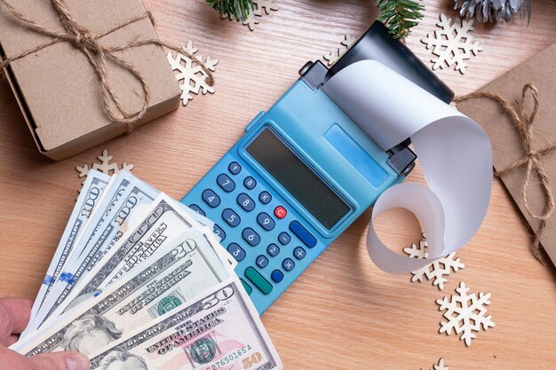 Buying gifts for Christmas and New Years - Cashier's hand holding cash dollars over the cash register for paying for Christmas gifts on the counter with decorated snowflakes