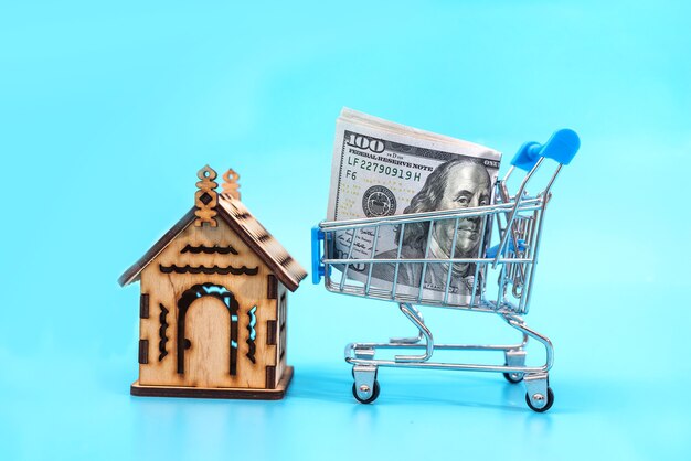 Buying a house and property, selling a house, real estate business concept, new house in a cart and dollars on a blue table.