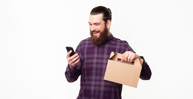 Buying online lunch box, cheerful man using smartphone and holding lunchbox