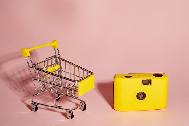 Buying photo equipment Yellow basket with yellow cameraBig purchases On a pink background A place for text