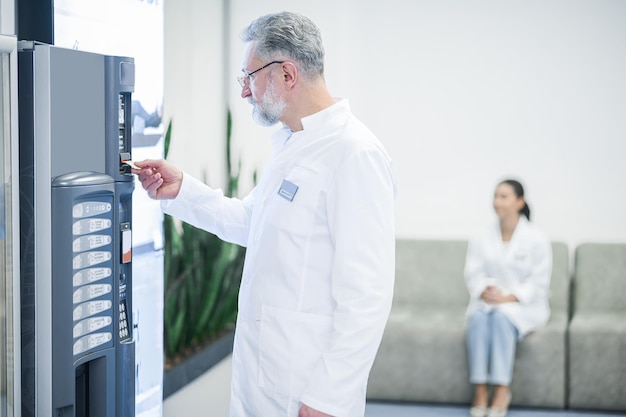 Buying a snack Grayhaired mature doctor standing near the slot machine