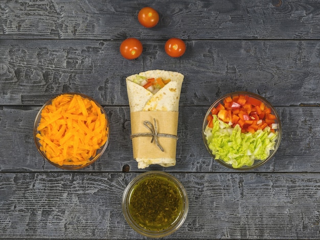 Cabbage, carrot, pepper, avocado, tomatoes in pita bread on a dark table