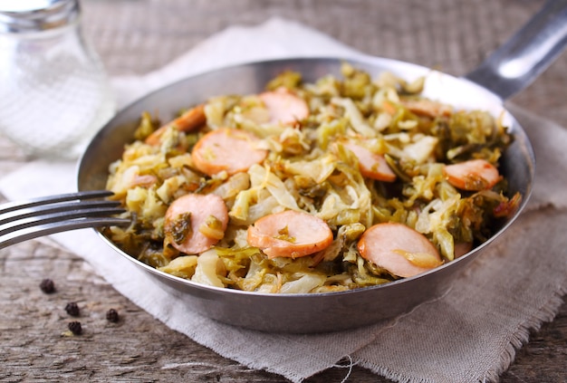 Cabbage stew with sausages in a frying pan on a wooden background