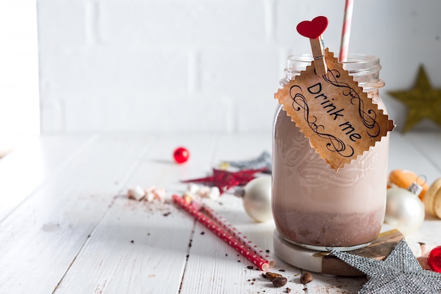 Cacao met marshmallow en rietjes in glazen pot met een bord Drink me