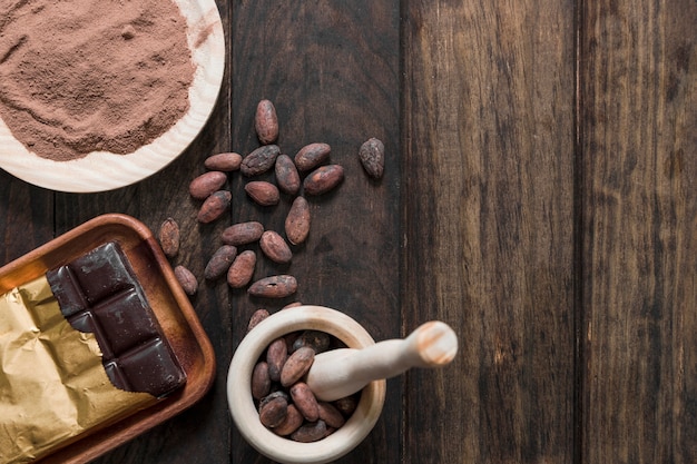 Cacaobonen met cacaopoeder en verpakte chocoladereep op houten lijst