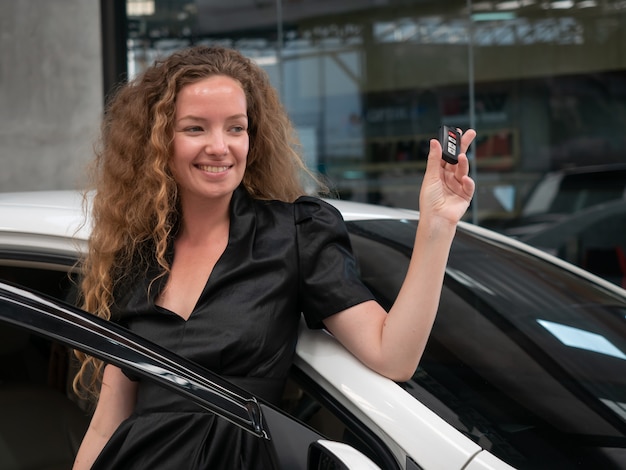 Cacausian vrouw die zich dichtbij een auto bevindt en autosleutels toont.