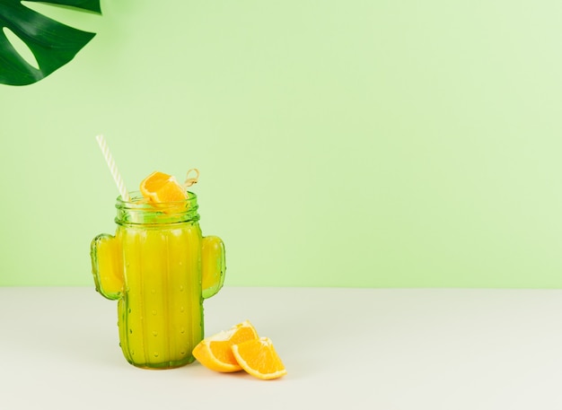 Cactus shaped glass with orange juice with green background. Copy space.