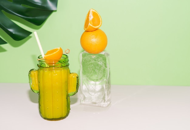 Cactusvormig glas met sinaasappelsap met fruitdecoratie op ijsblok. Ruimte kopiëren.