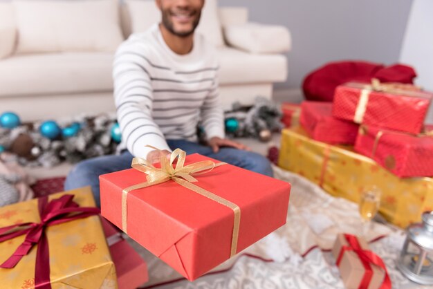 Cadeau voor jou. selectieve focus van een kerstcadeau dat wordt gewikkeld in een inpakpapier en wordt aangeboden terwijl het wordt vastgehouden door een positieve schattige jonge man