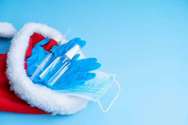 Cadeauset voor kerst en oud en nieuw 2021. Een hygiënische set van een medisch masker, handschoenen, een ontsmettingsmiddel en een spuit met een vaccin en een coronaviruschip in een kerstmanhoed. Vaccinatie 2021.