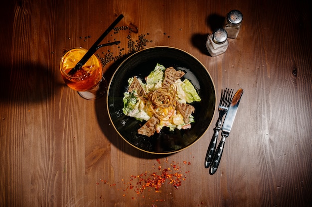 Caesar salad on black plate on wooden table.