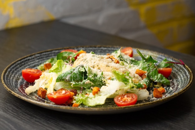 Photo caesar salad, in dark clay plate on wooden table