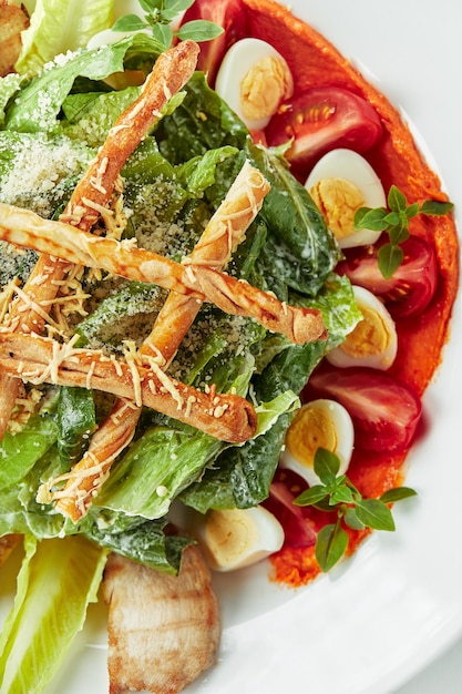 Caesar salad with bread sticks, quail eggs, cherry tomatoes and grilled chicken in plate on white background.