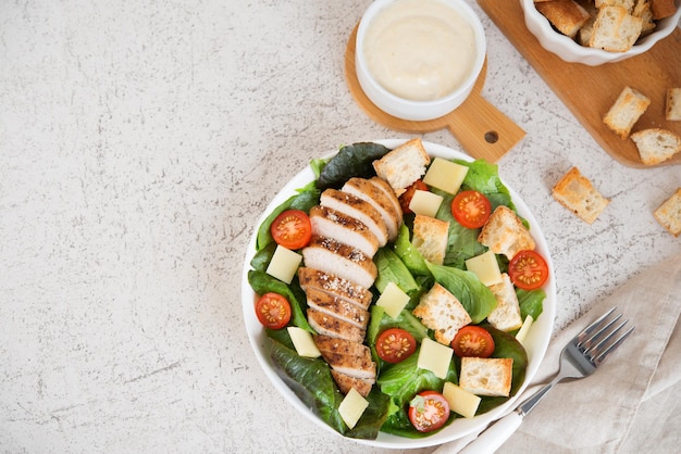 Caesar salad with chicken breast, cherry tomatoes, croutons and parmesan on a light background, top view, copy space