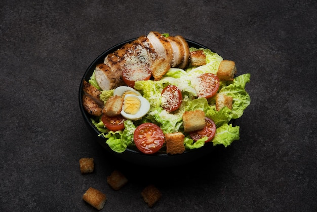 Insalata caesar con petto di pollo, pomodorini e parmigiano su fondo scuro, cena