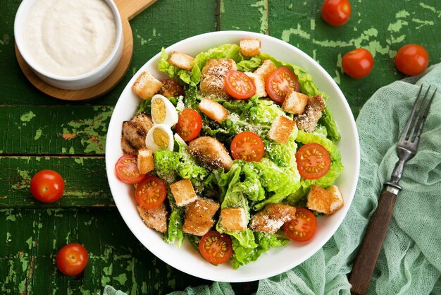 Caesar salad with chicken fillet, tomatoes, croutons and parmesan in a plate on a rustic wooden background, top view