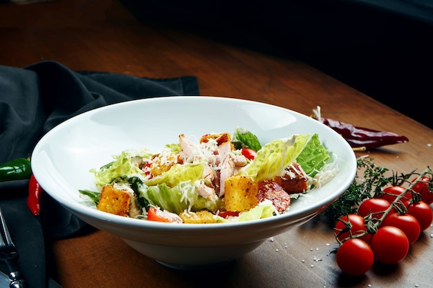 Caesar salad with croutons, parmesan, chicken, egg in white plate on wooden table. Restaurant serving. Close up