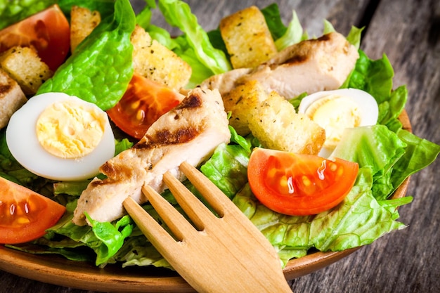 Caesar salad with croutons quail eggs cherry tomatoes and grilled chicken close up on wooden table