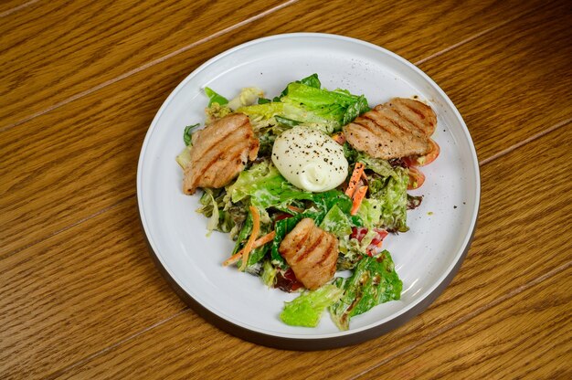 Caesar salad with croutons, quail eggs, cherry tomatoes and grilled chicken in wooden table.Delicious salad with chicken, nuts, egg and vegetables.