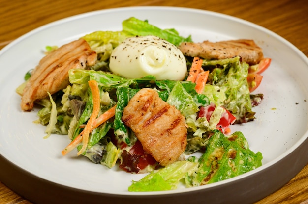 Caesar salad with croutons, quail eggs, cherry tomatoes and grilled chicken in wooden table.Delicious salad with chicken, nuts, egg and vegetables.