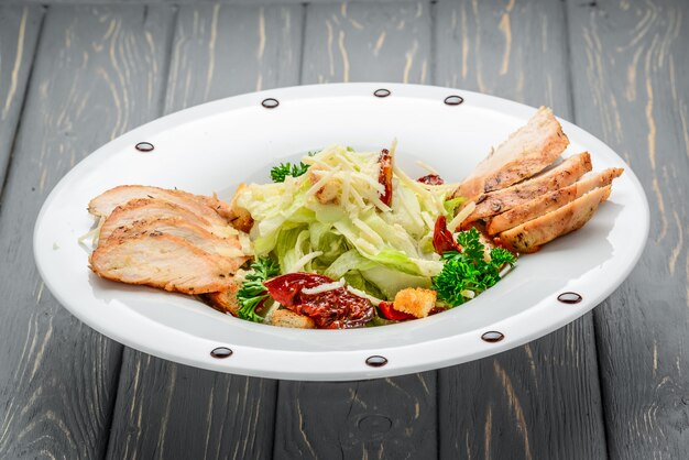 Caesar salad with croutons, quail eggs, cherry tomatoes and grilled chicken on a wooden table