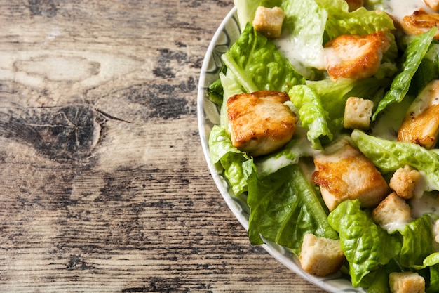 Caesar salad with lettuce,chicken and croutons on wooden table