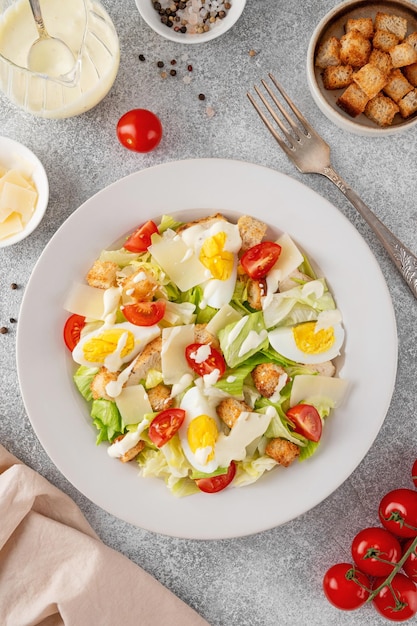 Фото Салат цезарь с салатами, жареной куриной грудью, вареными яйцами, помидорами, пармезанским сыром и крутонами.