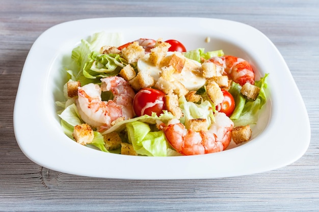 Caesar salad with prawns on white plate on table