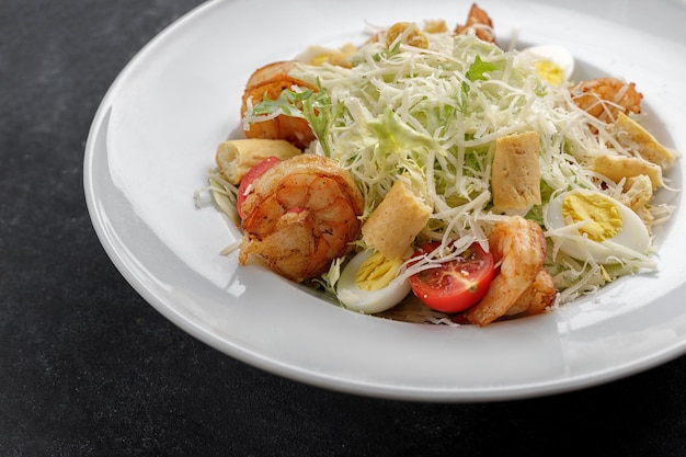 Caesar salad with shrimps on a dark background