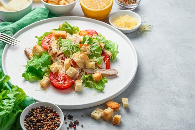 Caesar salade close-up op een witte plaat, omringd door ingrediënten op een grijze achtergrond. Het concept van gezonde voeding.