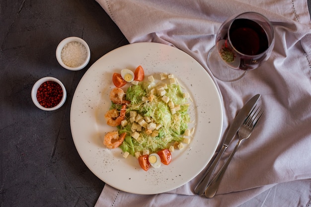 Caesar salade met garnalen en glas wijn, zout en peper op tafel.