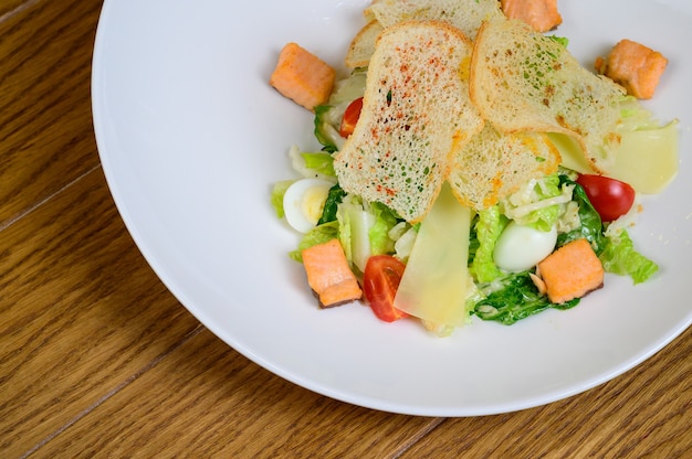 Caesar salade met zalm op witte plaat op houten achtergrond.Caesar salade met zalm, bovenaanzicht