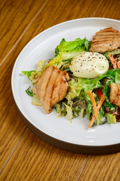 Caesarsalade met croutons, kwarteleitjes, kerstomaatjes en gegrilde kip in houten tafel. heerlijke salade met kip, noten, ei en groenten.