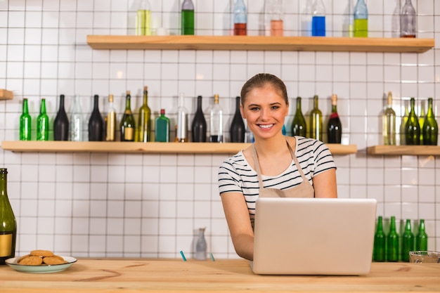 In the cafe. Delighted joyful nice woman smiling and looking at you while using laptop for work