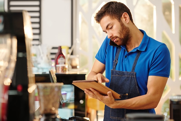 Cafe owner talking on phone with customer and taking notes on tablet computer