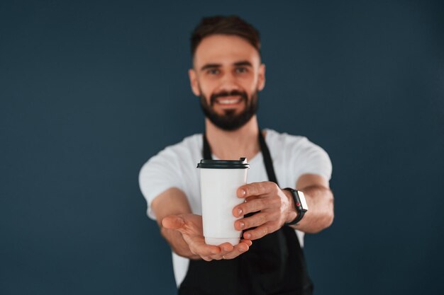 Foto l'operaio del caffè è in grembiule l'uomo bello è nello studio sullo sfondo blu