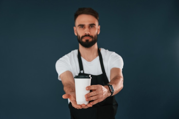 Photo cafe worker is in apron handsome man is in the studio against blue background