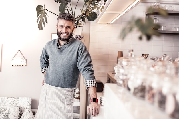 Cafeteria owner. Pleasant delighted man standing near the counter while smiling to you