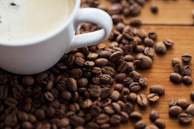 caffeine, objects and drinks concept - close up coffee cup and beans on wooden table