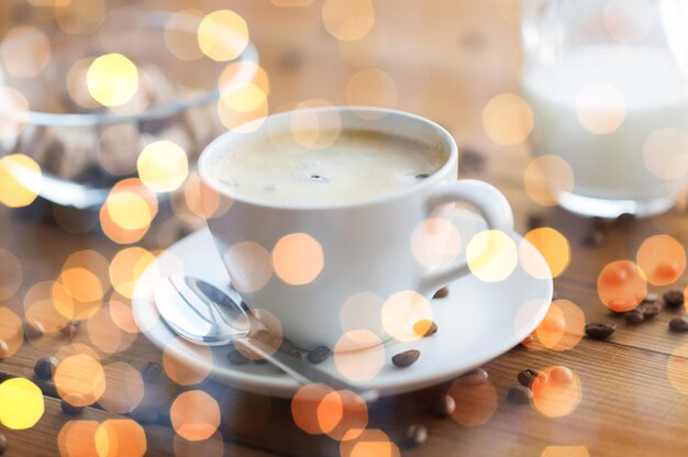 caffeine, objects and drinks concept - close up coffee cup and grains on wooden table