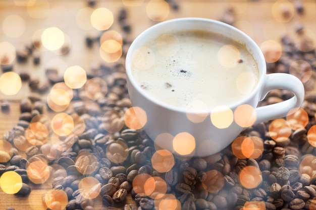 caffeine, objects and drinks concept - close up coffee cup and grains on wooden table