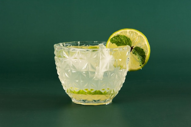 Photo caipirinha glass of pinga cocktail with ice and lime on a smooth green background in front photo