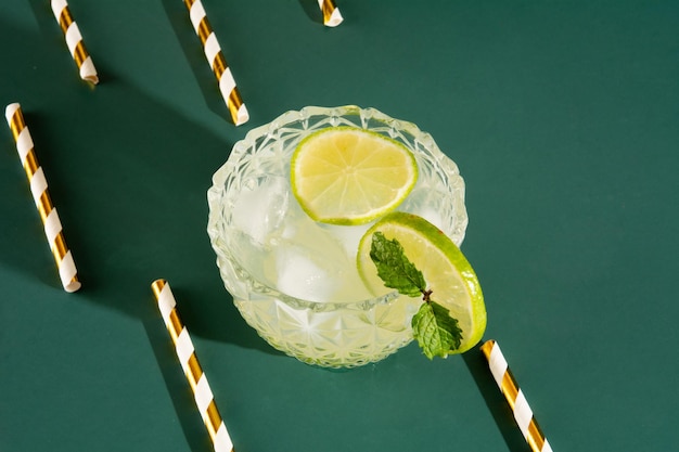 Caipirinha glass of pinga cocktail with ice and lime on a smooth green background with lemon aerial top view photo