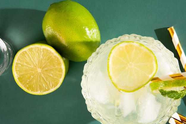레몬 위쪽 사진과 함께 매끄러운 녹색 배경에 얼음과 라임으로 된 핑가 테일의 Caipirinha 컵