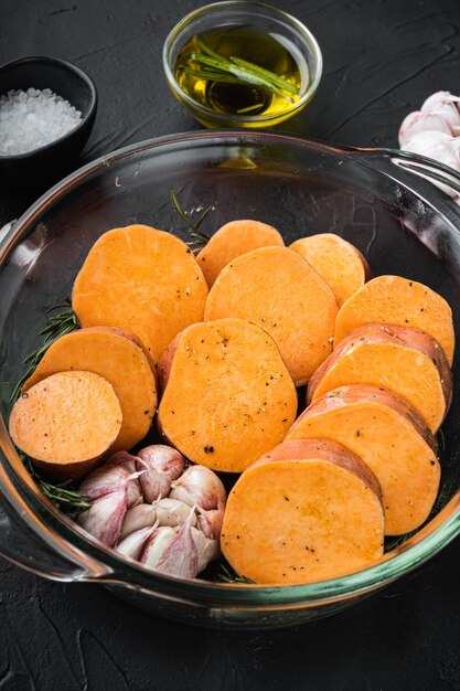 Cajun sweet potatoes for baking with herbs and spices on black background.